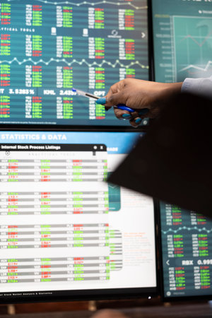 Black woman and pointing at a digital monitor with a pen, analyzing stock market buy and sell data. African American female entrepreneur highlighting forex trading movements on multiple screens.の写真素材