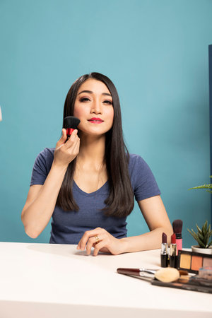 Warm and engaging beauty influencer hosting a live online makeup tutorial, showcasing various brush techniques. Asian content creator broadcasting from her studio, discussing cosmetic tools.の写真素材
