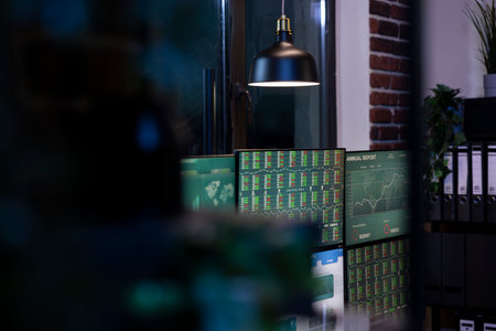 Quiet, dark office with multiple monitors displaying charts, creating an atmosphere of anticipation for upcoming trading session. Professional trading workspace, arranged for night shift employees.の写真素材