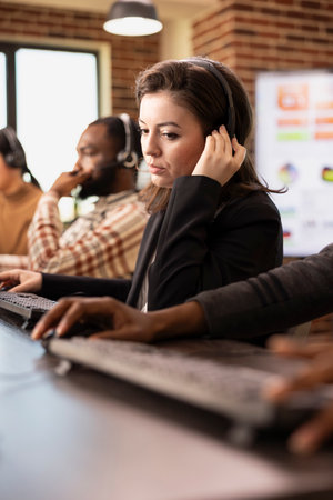 Caucasian customer service agent wearing hands free headset concentrates on delivering technical support. Closeup of young female employee adjusting her headphones while assisting remote client.の写真素材