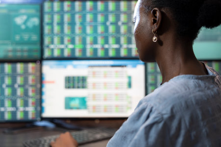 African american female investor monitoring forex trading charts on multiple monitors, deeply engaged in reviewing company shares and market movements. Black woman analyzing stock exchange status.の写真素材