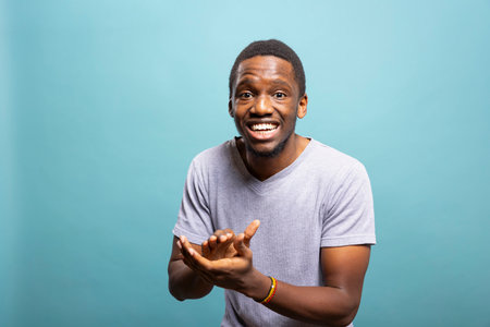 African american man with proud expression leaning forward and clapping his hands, happy with the good news. Young black guy standing against blue background, looking at camera and giving an applause.の写真素材