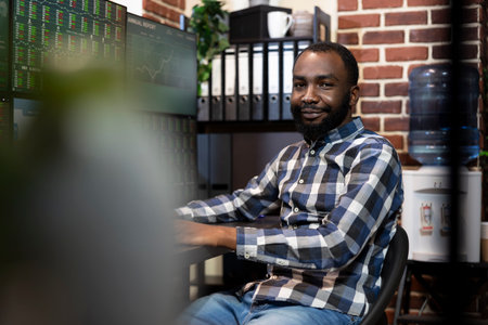 Black businessman sitting and smiling at camera, ready to analyze financial data on multiple...