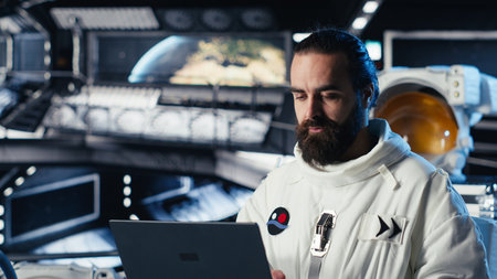 Astronaut using laptop to verify mission parameters after completing planet surface expedition. Cosmonaut manages systems using notebook, leaving Mars, updating flight log to return homeの写真素材