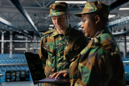 Teamworking soldiers in server hub doing brainstorming, checking reports on laptop. Team of army information experts working together, monitoring systems using notebook in data centerの写真素材
