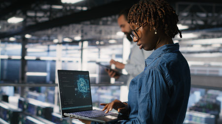 System administrators in data center monitoring AI LLM visualization. African american server farm coworkers overseeing rigs powering machine learning processesの写真素材