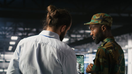 Military technician reviewing tactical dashboard on laptop screen inside secure server hub. Army expert using strategic communications and infrastructure oversight software on notebookの写真素材
