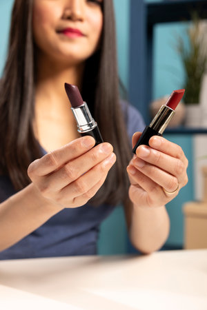 Selective focus on various lipstick shades held by a beautiful woman, showcasing them to the camera during her vlogging session. Closeup of makeup products presented by an asian beauty blogger.の写真素材