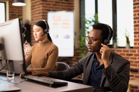 Black male entrepreneur wearing a headset, attentively listening during an online marketing presentation. African American wheelchair user communicating with clients in a brick walled office.の写真素材