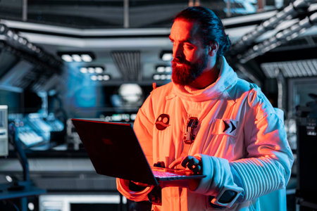 Cosmonaut works on laptop to troubleshoot red light warning triggered by system error in orbital...