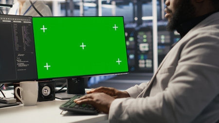 Data center admin inspecting gear using green screen mockup PC, doing maintenance tasks. African american server farm worker using chroma key computer, conducting system checks, camera Aの写真素材