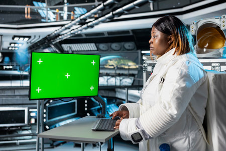 Astronaut reviewing spacecraft analytics on green screen monitor to ensure safe operation during long distance space travel. Woman in orbit station uses mockup display during cosmic journeyの写真素材