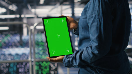 Data center worker using green screen mockup tablet, doing maintenance on rigs handling AI tasks. Server hub admin using chroma key device to manage storage arrays supporting deep learningの写真素材