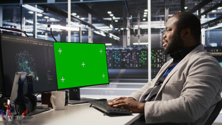 Data center programmer working on green screen desktop PC, updating storage infrastructure. IT specialist using mockup computer in server hub workspace filled with networking tech, camera Aの写真素材