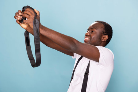 African american male photographer captures a personal moment, taking a picture of himself with his camera. His casual outfit and expressive pose create a compelling and engaging portrait.の写真素材