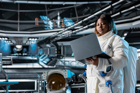 Astronaut using laptop to confirm suit integrity, monitoring life support systems. Orbital station crew member testing gear during routine equipment check using notebook, conducting safety checksの写真素材