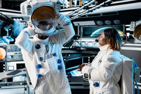 Researcher travelling in space with starship putting helmet on, talking with colleague, conducting scientific experiments. Scientist dressing in equipment, chatting with coworker during cosmic journeyの写真素材