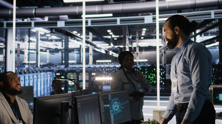 Data center worker looking at workstation with other engineers in background. Programmer working in...