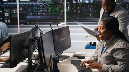Scared technician in server room responding to hacking detection, requesting help from colleagues to protect critical data. Engineering team alerted by suspicious virus attack activity logs, camera Aの写真素材