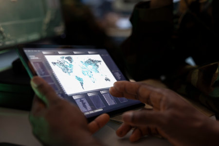 Military officer conducts tactical reconnaissance in war room, utilizing tablet for data analysis. Army professional uses satellite tech on digital device to look at aerial map, pinpointing targetsの写真素材