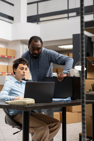 Team of diverse workers reviewing custom orders in a distribution hub filled with taped boxes on shelves or racks, People representing a local brand small scale logistics center.の写真素材
