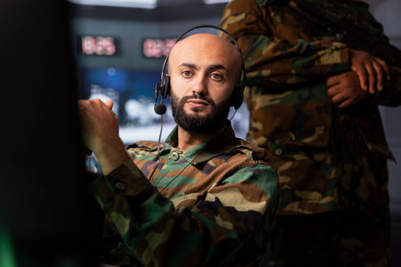 Military agent in war room doing reconnaissance mission, using headset gear. Army expert monitoring counterinsurgency enemy fighters using telecommunication systems to intercept callsの写真素材