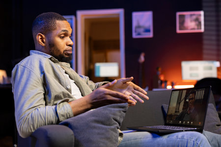 African american web user meeting with workmates on a video call remotely, ensuring a strong discussion via wireless connection. Freelancer joining an executive conference from his loftの写真素材
