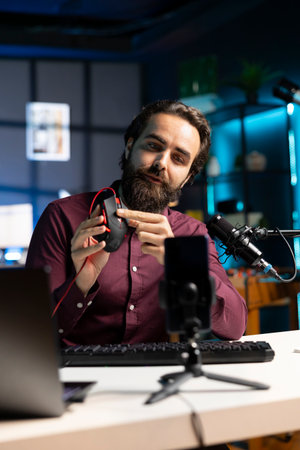 Tech specialist filming video review for internet channel in apartment studio, analyzing wired gaming mouse for his audience. Media star endorsing computer peripheral deviceの写真素材