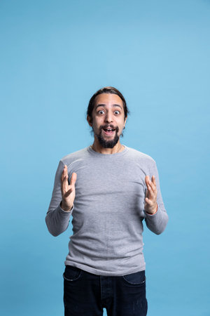 Surprised ecstatic young person with a cool joyful attitude in studio, feeling satisfied and enthusiastic about something against blue background. Smiling confident man feeling excited.の写真素材