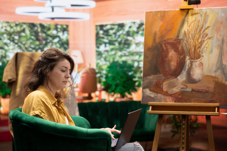 Painter searching for fine art inspiration online in her art and craft atelier, doing creative process research for a contemporary masterpiece. Woman spending quality time in workshop.の写真素材