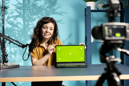 Cheerful woman in studio filming tech tutorial on how to do maintenance on broken chroma key laptop. Jolly online show host teaching subscribers how to open and fix defective green screen notebookの写真素材