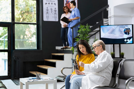 Skilled physician gives advice and explanation of x ray scans to asian patient during a health check in a hospital lobby. Specialist analyzes radiology test results for a recovery plan.の写真素材