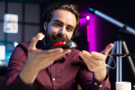 Influencer happily promoting neon lit gaming mouse from sponsor to audience. Joyful content creator paid by brand to showcase computer peripheral device, recording with professional microphoneの写真素材