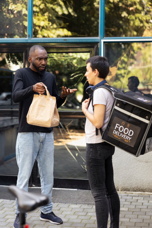 Black male client holding a takeout package with the wrong order, confronting the delivery worker about a shipping problem. The incorrect meal causes tension during failed courier service.の写真素材