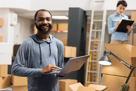 African american man overseeing product shipment and order logistics, working in small scale factory operations with taped boxes stacked on shelves. Handling goods and processing orders.の写真素材