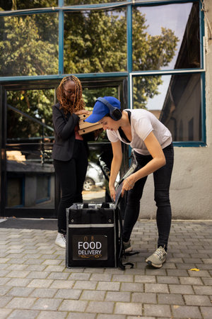 Woman courier handing massive stack of pizzas to a customer. Employee completing the restaurant delivery with attention and professionalism, ensuring express takeaway service.の写真素材