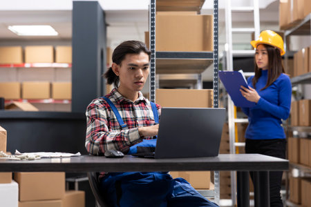 Asian startup employee applies labels and organizes merchandise for delivery. Man sitting at the packaging station to handle all custom orders, small scale fulfillment center. Local brand.の写真素材