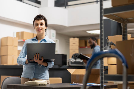 Woman employee working in a warehouse on order processing in small business depot, preparing taped boxes for local brand express delivery logistics. Distribution center supply room.の写真素材