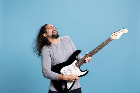 Enthusiastic rocker playing a black electric guitar with passion and joy for rock and roll music. Dynamic, trendy performer with long hair brings movement, fun and entertainment to the studio.の写真素材
