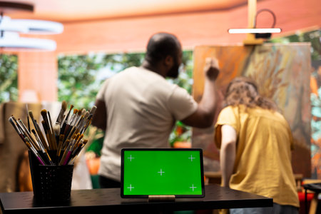 Diverse artists painting a new artwork next to isolated mockup screen, collaborating on a masterpiece for fine art gallery exhibition. Painter and apprentice using watercolor paints on canvas.の写真素材
