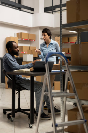 Diverse team at desk discussing order processing to guarantee distribution in a tightly packed storage room filled with products and boxes. Organized structure of a small scale business.の写真素材