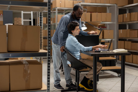 Multiethnic staff uses distribution hub logistics for order processing, coordinating logistics in a small warehouse. Solving business operations and tasks of a local delivery company.の写真素材