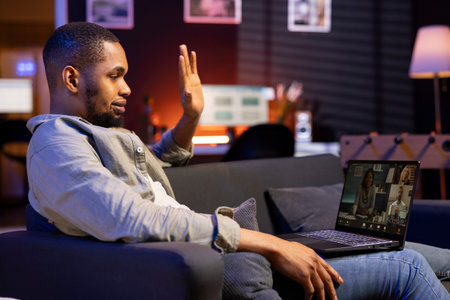 African american web user meeting with workmates on a video call remotely, ensuring a strong discussion via wireless connection. Freelancer joining an executive conference from his loftの写真素材