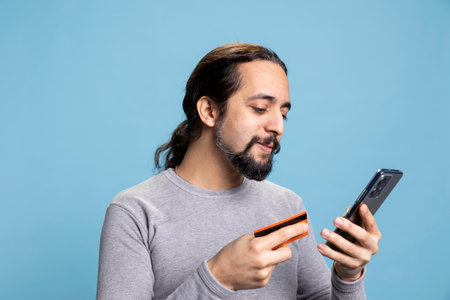 Happy bearded man making a secure online purchase with a smartphone and credit card. Young guy using his e wallet for mobile banking and digital transactions, spending money on web.の写真素材