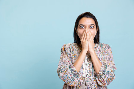 Anxious indian woman covering her face with palms and being worried about the future, getting concerned against studio background. Tense person shocked by troubling news and gasping.の写真素材