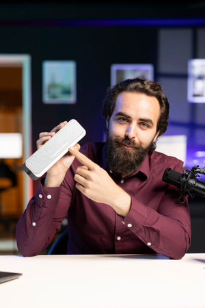 Joyful influencer doing technology review of wireless portable speaker for internet platforms channel. Influencer pointing to music playing gear to his subscribers, recommending itの写真素材