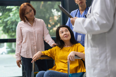 Healthcare medic supporting woman in wheelchair during routine appointment at inclusive clinic. Expert offering advice on maintaining wellness and adapting lifestyle around physical disability.の写真素材