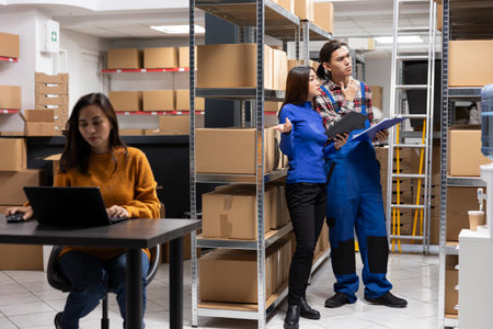 Asian team of workers in a depot checking the packages for shipment logistics, overseeing express delivery for orders. Staff focusing on growing the local brand small business.の写真素材