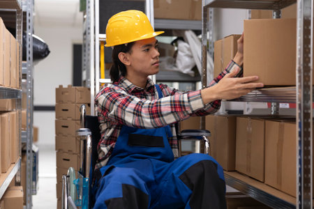 Asian employee with physical impairment processing parcels for local delivery, checking inventory and packages on depot racks. Storage room and shelves designed for accessibility.の写真素材