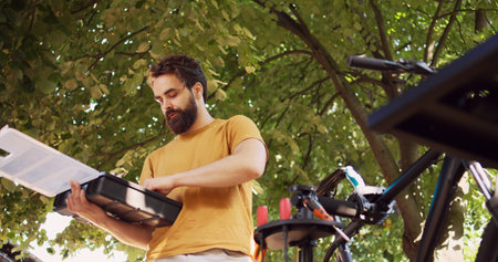 Motivated caucasian man diligently organizing specialized equipment from toolbox for bike maintenance in yard. Dedicated young male arranging professional work tools on bicycle repair-stand.の写真素材